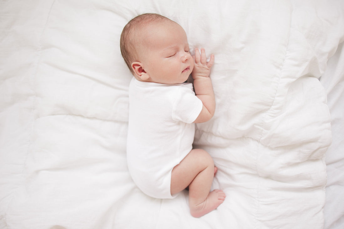Sleeping newborn baby in white bodysuit laying on a white blanket