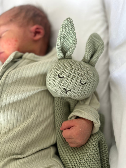 Newborn baby sleeping, wearing organic cotton sage sleepsuit and holding organic cotton sage bunny comforter