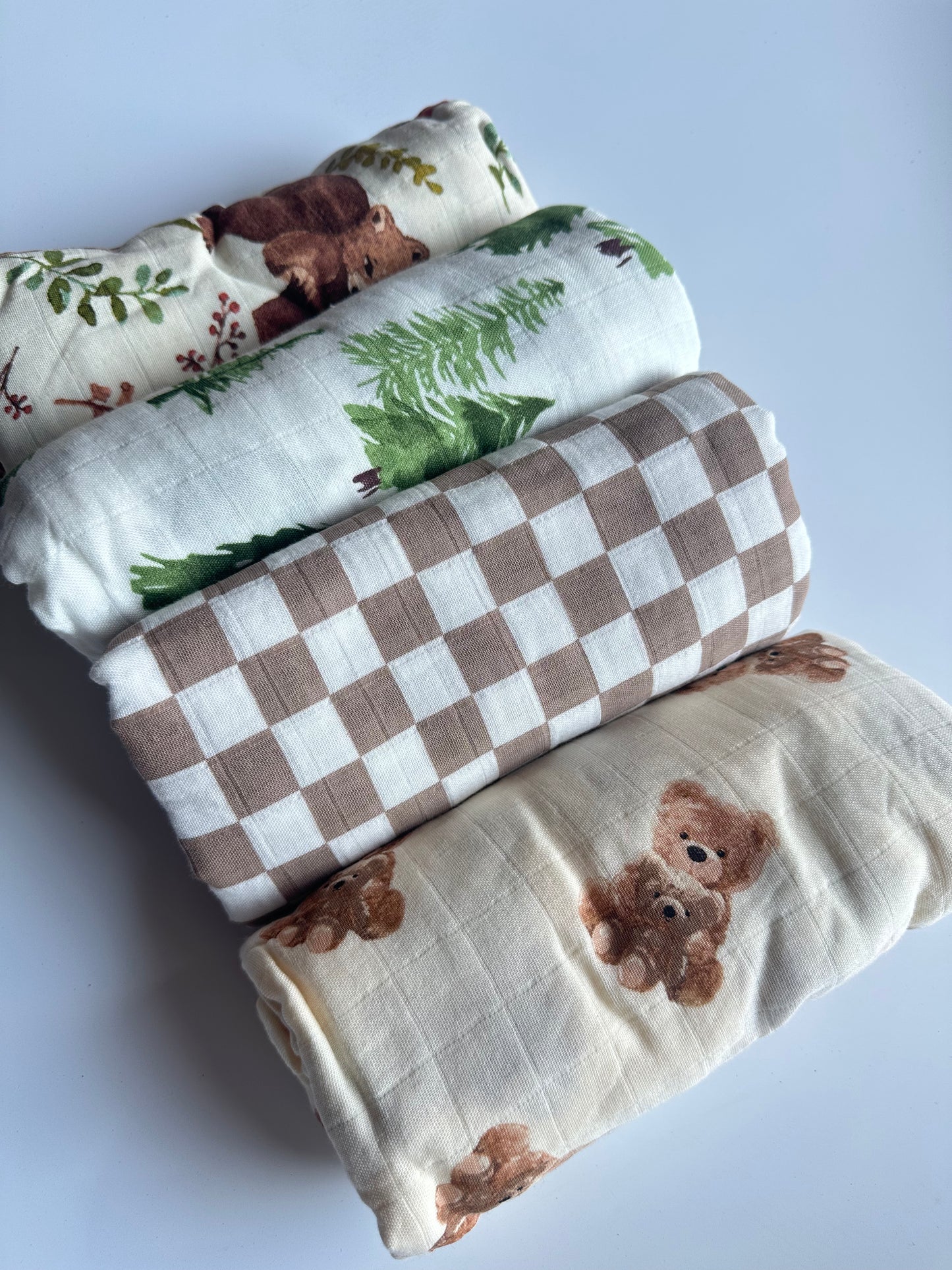 4 patterned muslin swaddle blankets rolled up and laid out on a white background