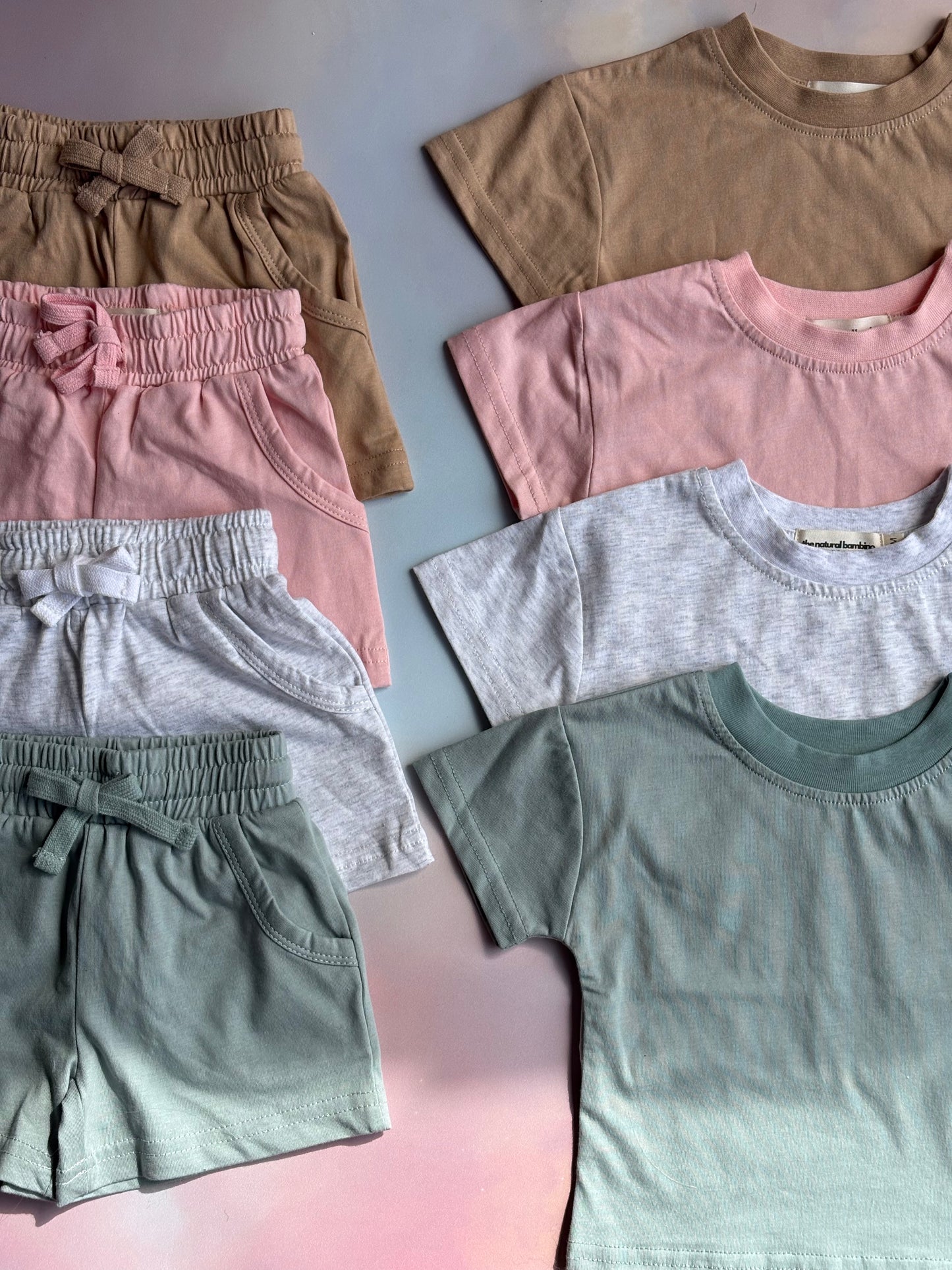 T-shirt and shorts sets laid out on a pink/blue background