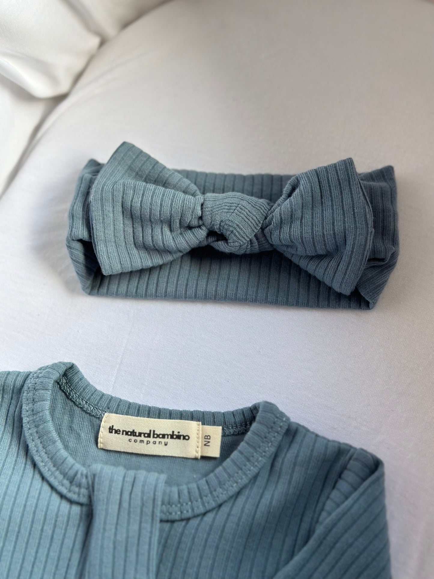 blue baby bow headband laid in a moses basket next to a matching sleepsuit
