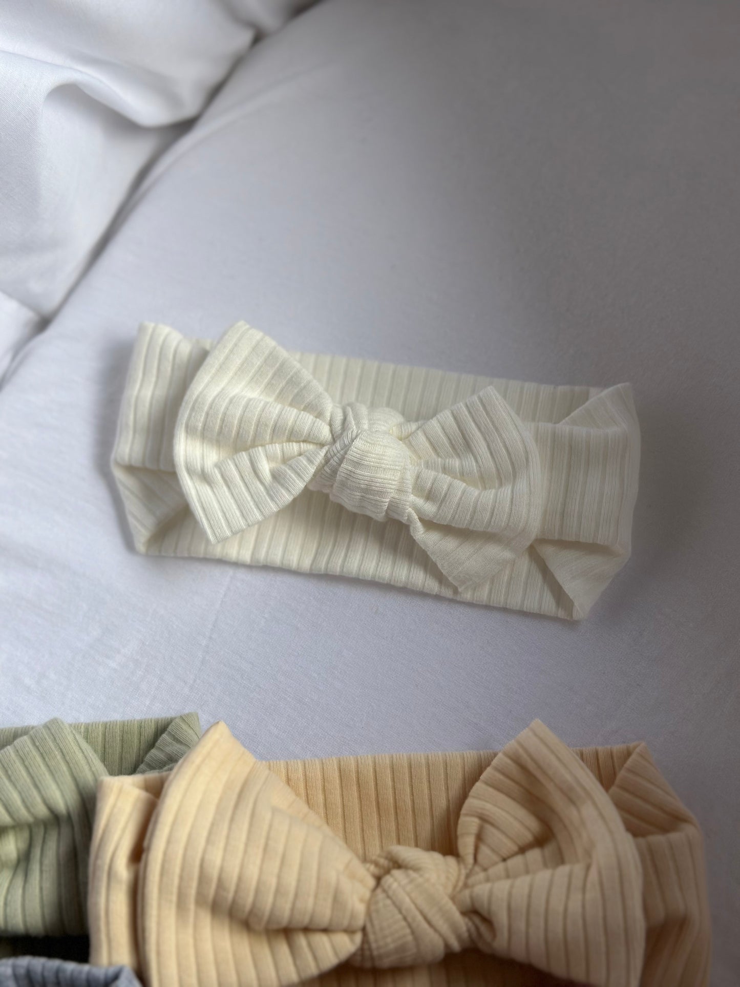 white baby bow headband laid in a moses basket next to other headbands