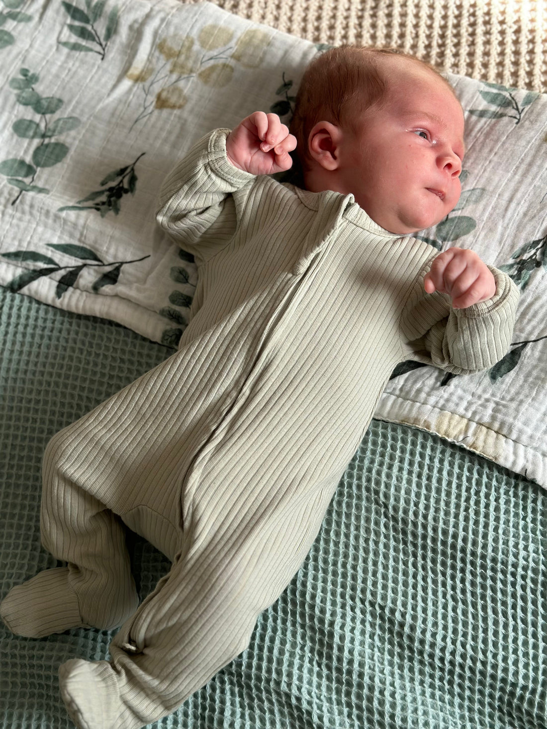 Newborn baby wearing organic cotton sage sleepsuit, laying on a green bamboo blanket