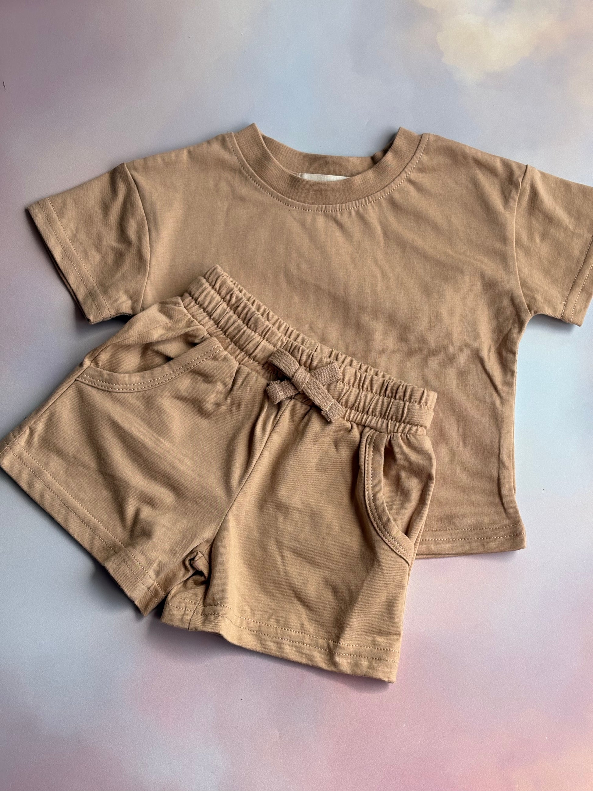 beige t-shirt and shorts set laid out on a coloured backdrop 