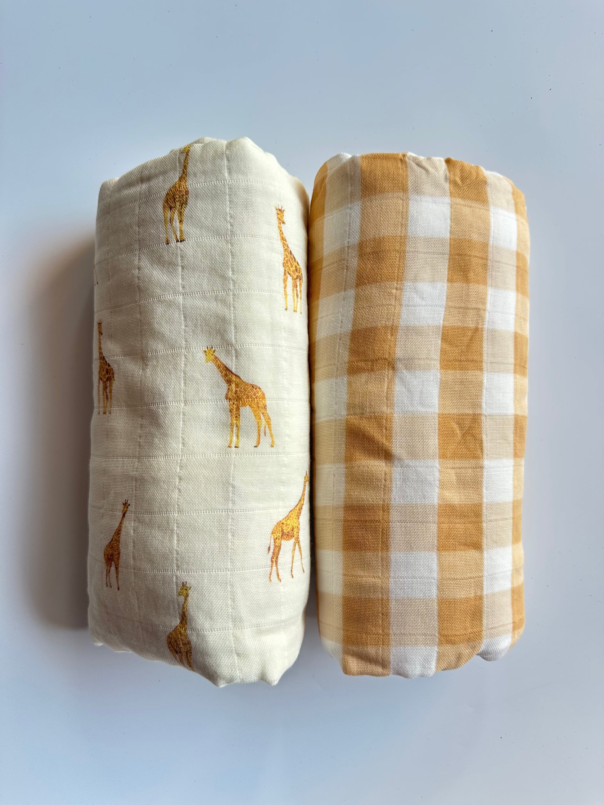 Rolled up giraffe and yellow checkered muslin blanket, placed on white background