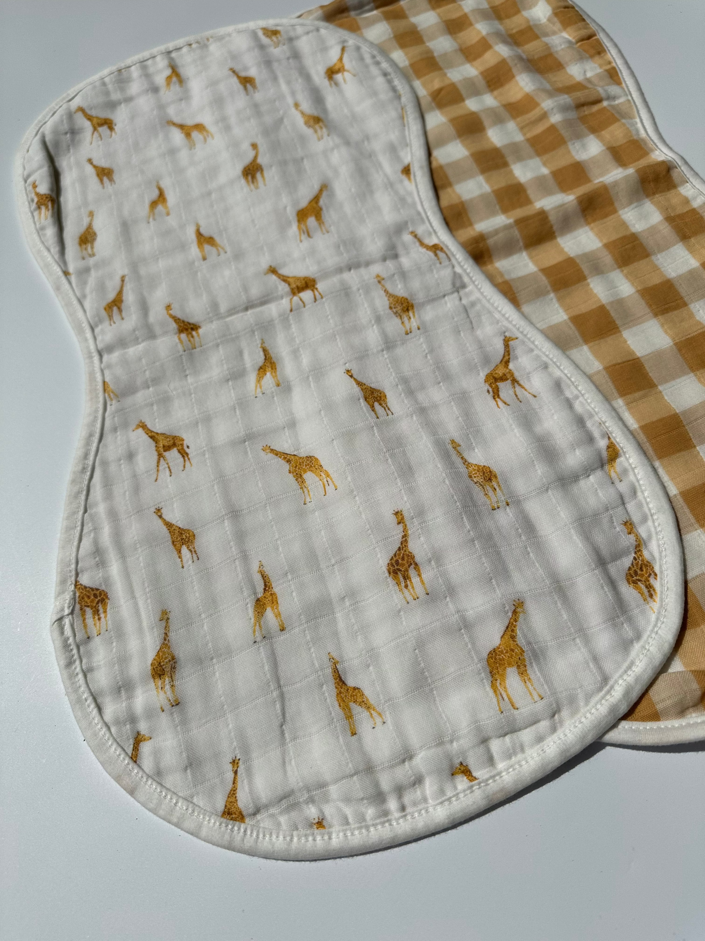 Set of 2 Yellow checkered and giraffe muslin burp cloth laid out flat on a white background