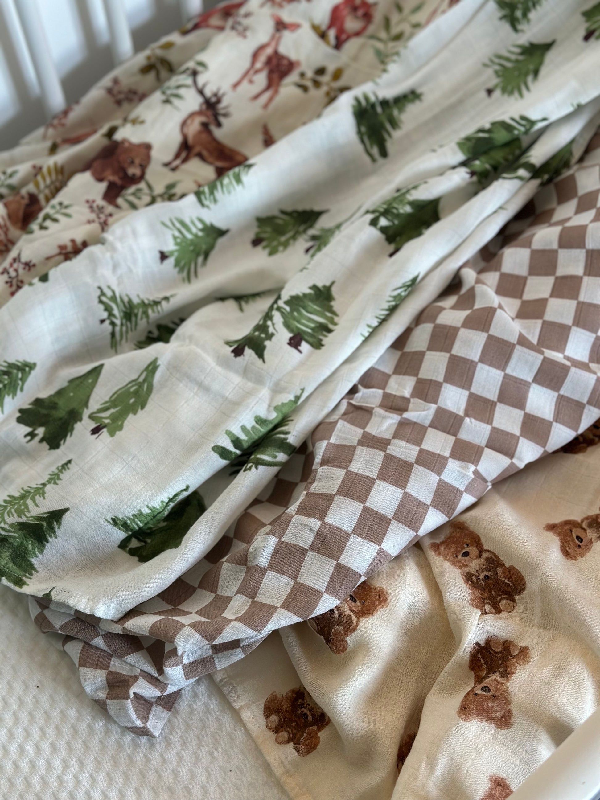 4 patterned muslin swaddle blankets laid out in cot