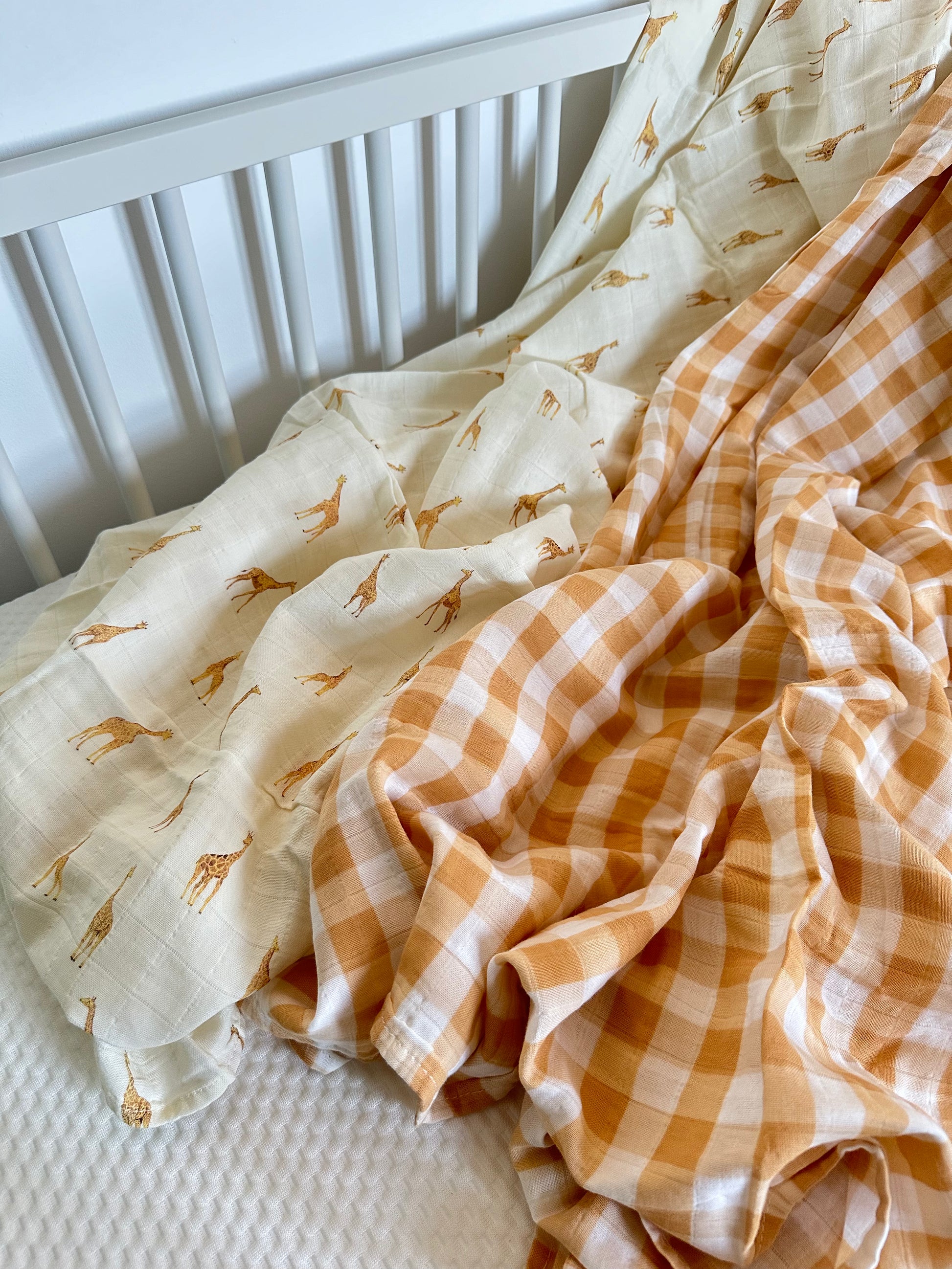Yellow checkered and giraffe muslin swaddle blankets laid out in white cot