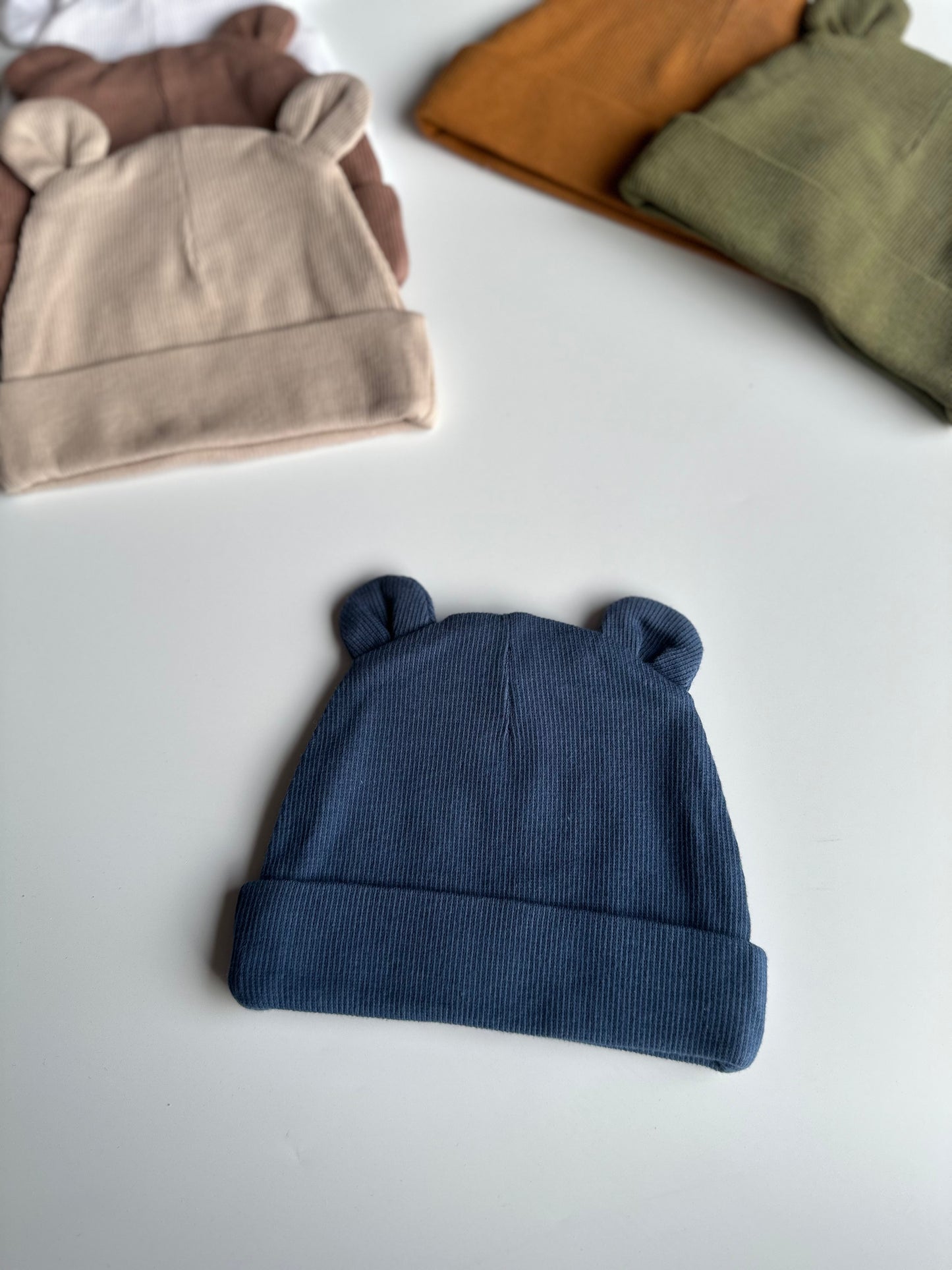 Infant bear hat in navy, laid out on white background with other newborn hats in the background