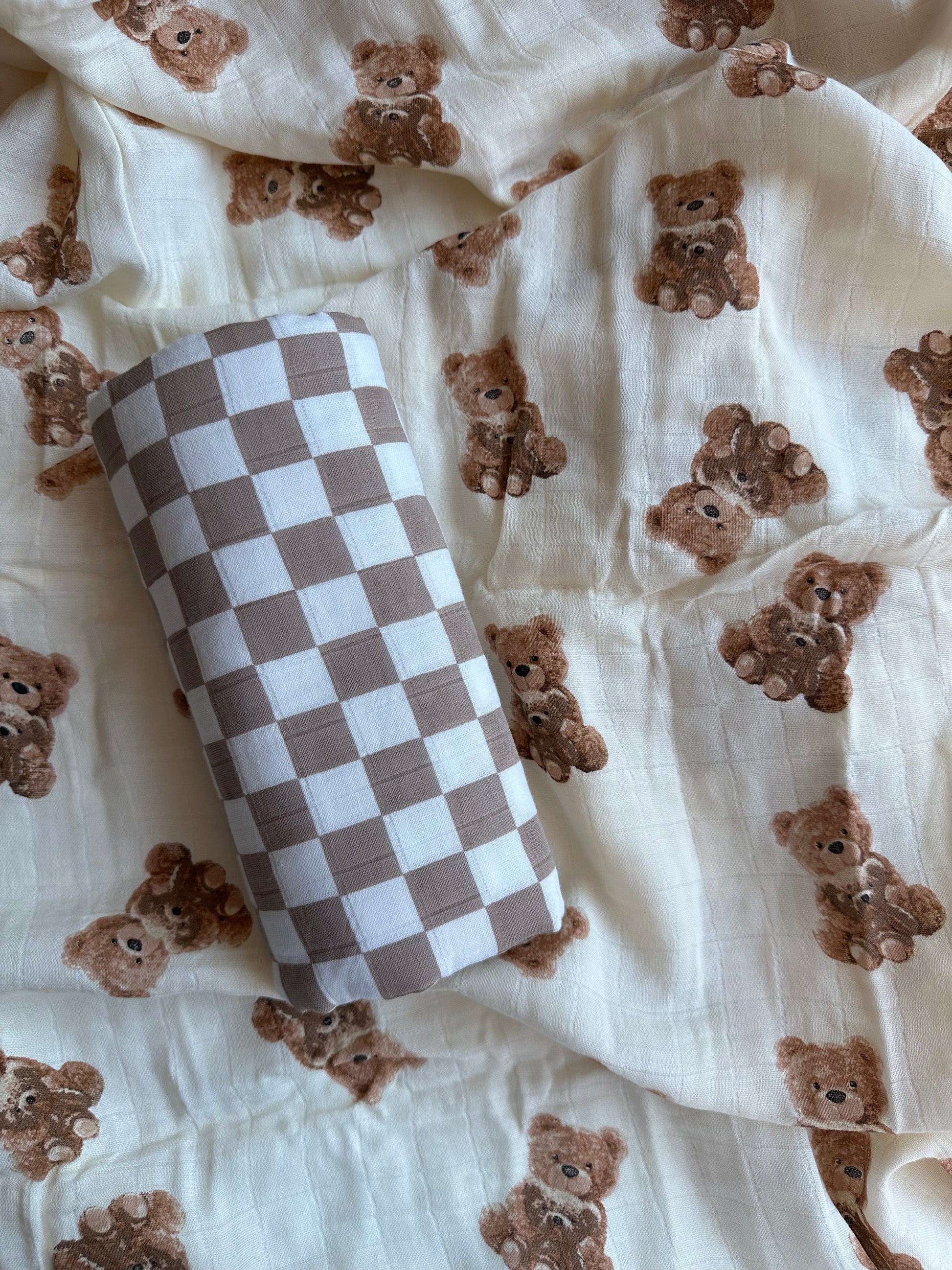 brown checkered muslin swaddle blanket rolled up and placed on bear muslin blanket