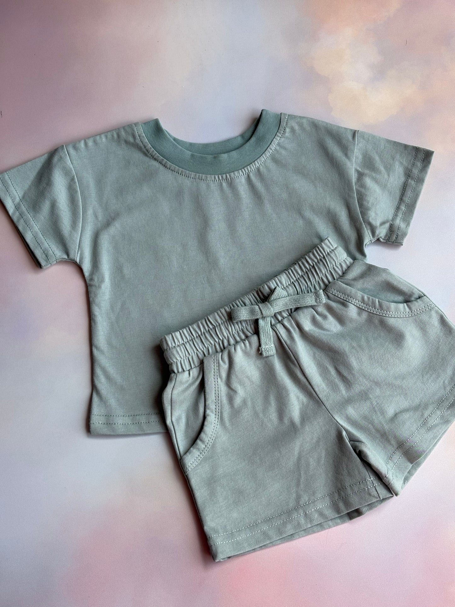 green t-shirt and shorts set laid out on a coloured backdrop 