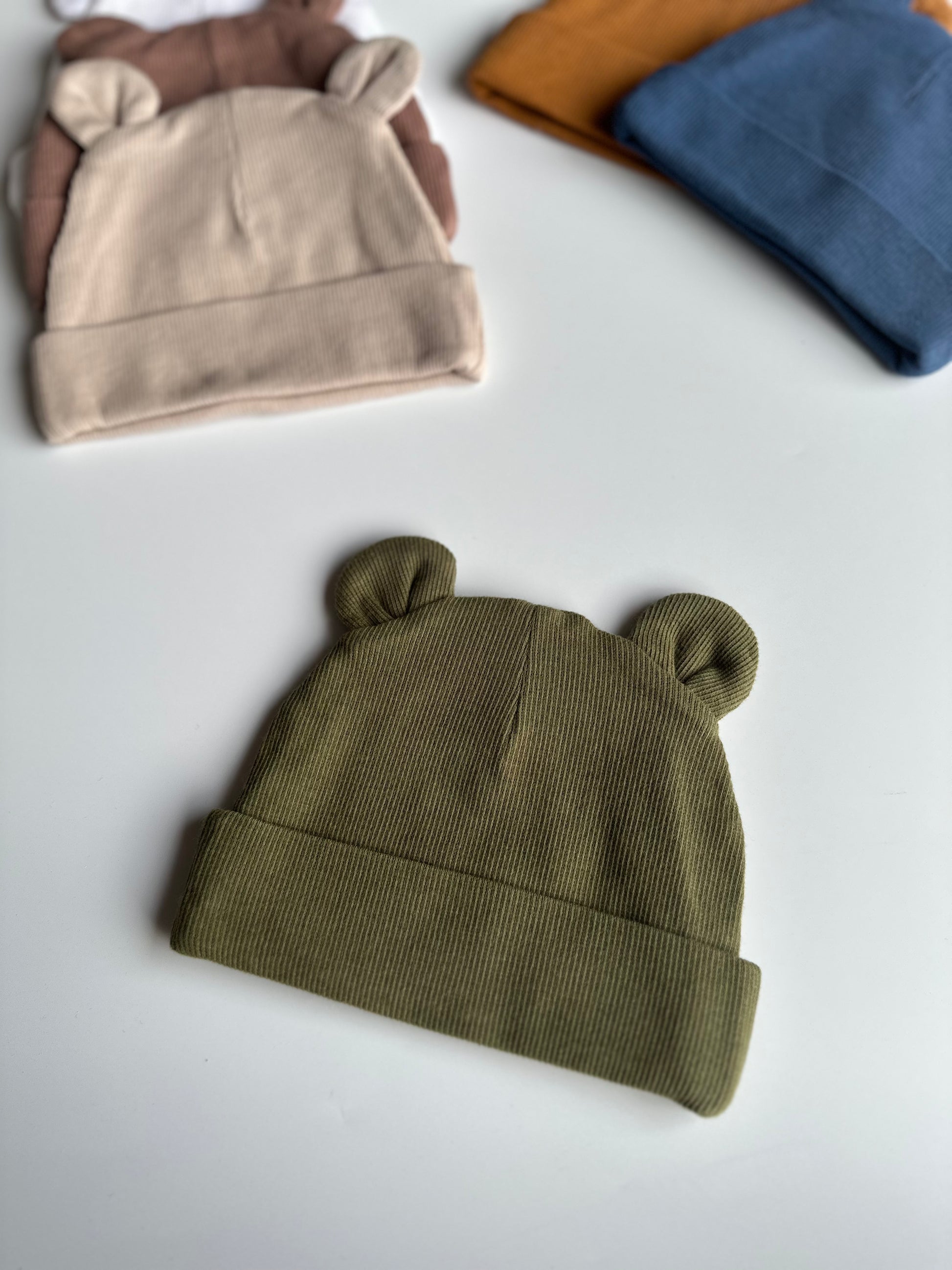 Infant bear hat in khaki, laid out on white background with other newborn hats in the background